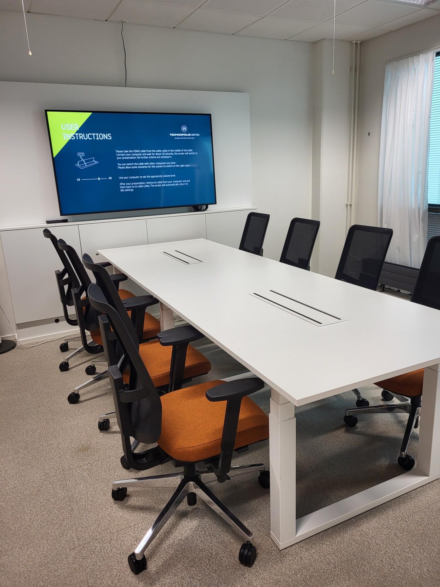 A stylish meeting room on the third floor, with a window overlooking a cozy and bright restaurant. The room features a boardroom-style table for 8 people, wireless internet access, an LCD screen, and a flip chart.