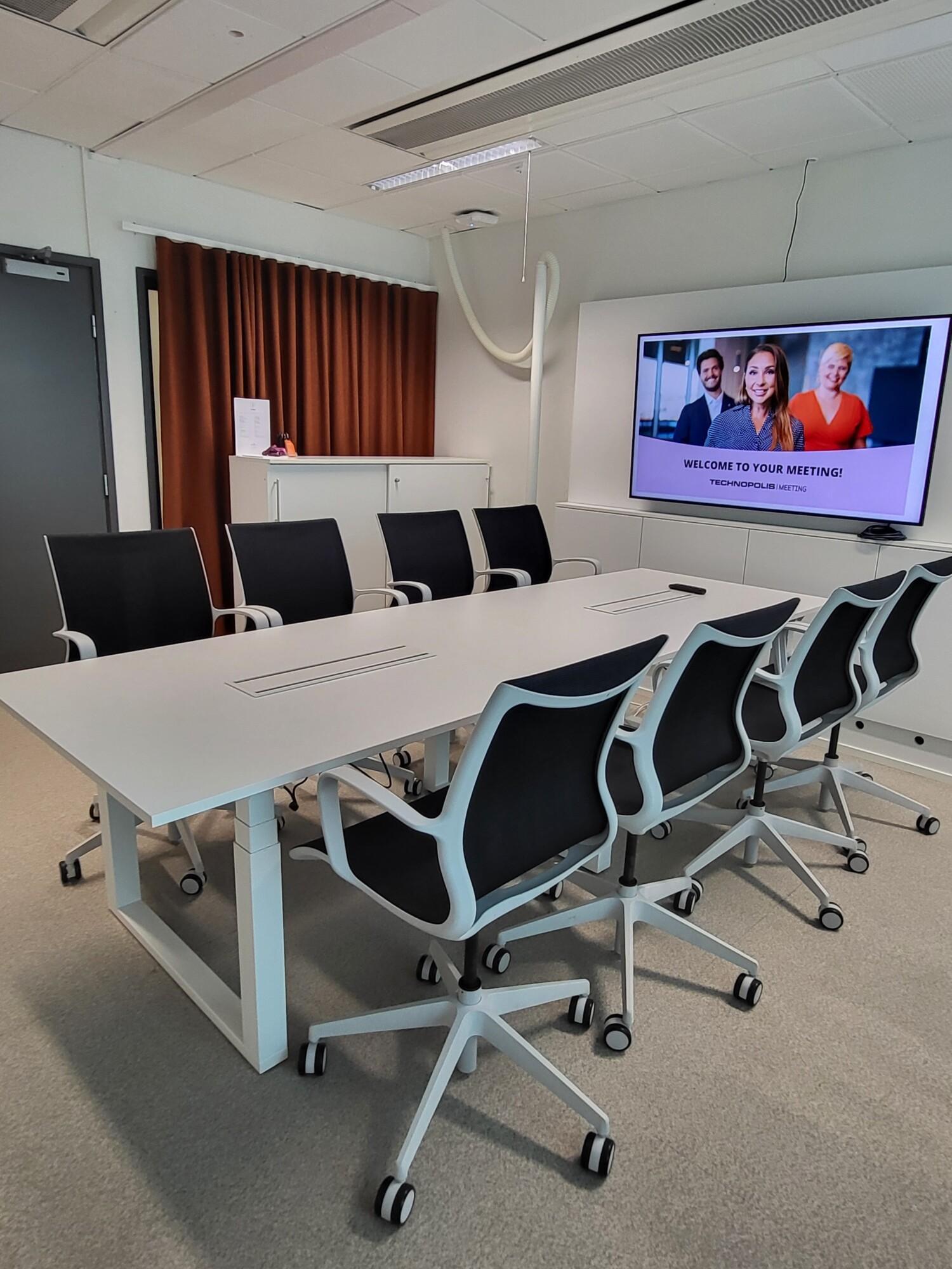 A stylish meeting room on the third floor, with a window overlooking a cozy and bright restaurant. The room features a boardroom-style table for 8 people, wireless internet access, an LCD screen, and a flip chart.